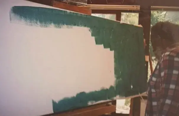 Johnson in a checked shirt painting a large canvas with green bands of color