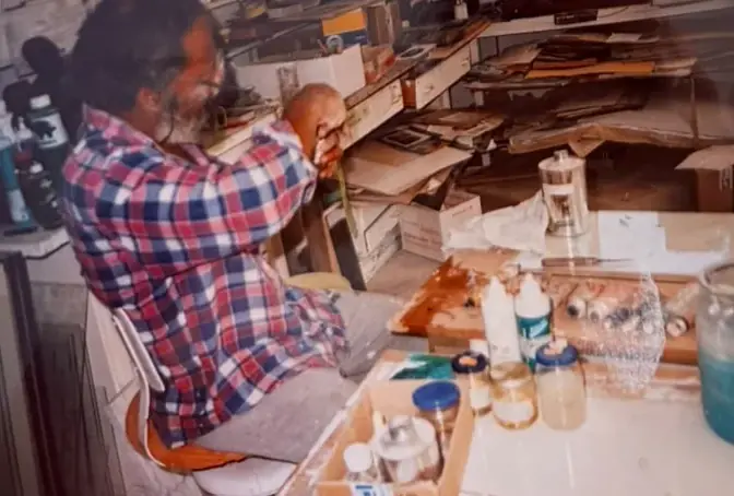 Johnson at his workbench among shelves, paint bottles and papers