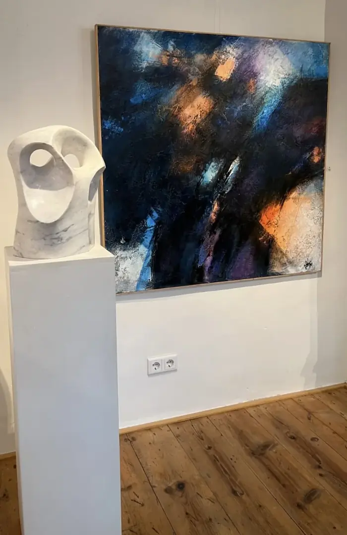 Dark blue painting on a white wall, with a white marble sculpture on a pedestal in front of it