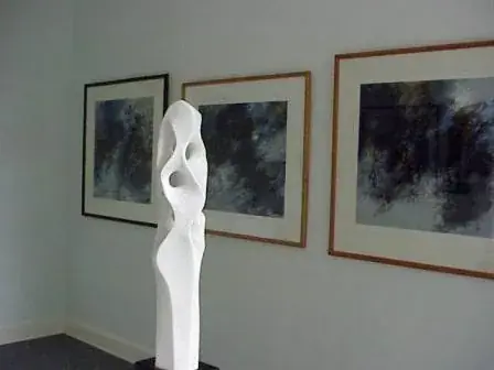 Exhibition room with a tall white sculpture and framed dark paintings