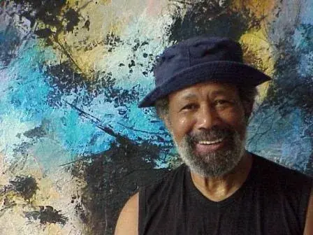 Johnson in 2003 in a blue hat and black shirt in front of one of his blue and yellow paintings, smiling