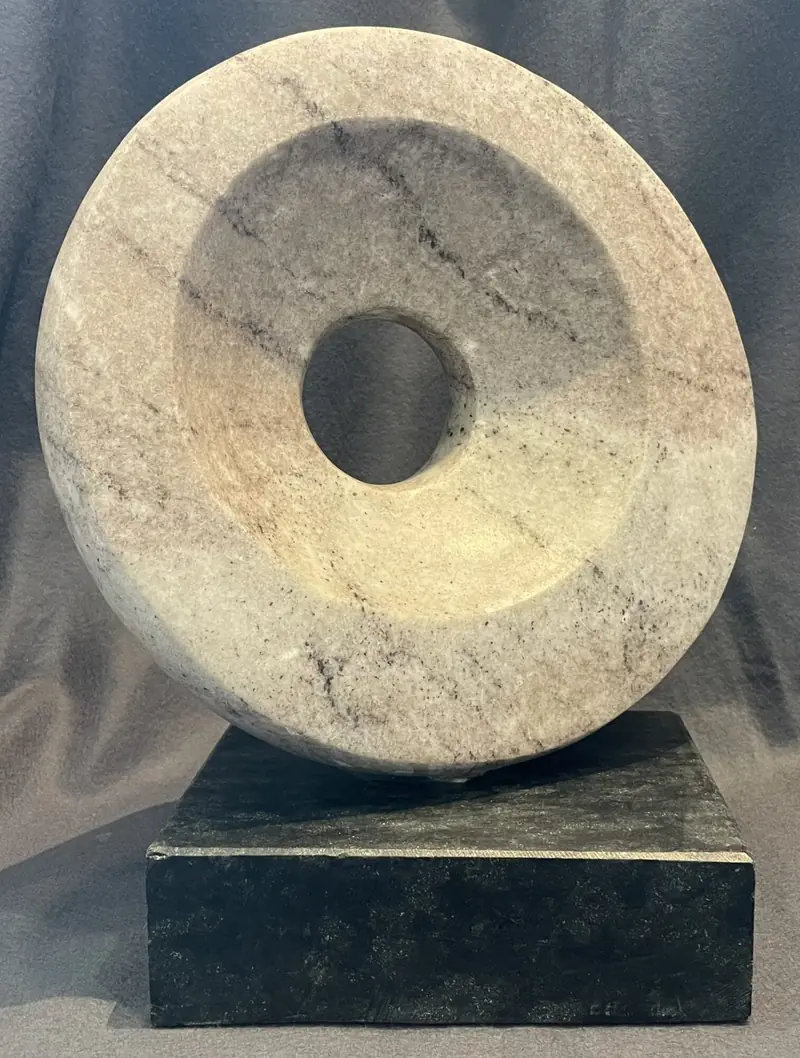 Ring-shaped sculpture of pale, gray-veined marble on a dark stone base